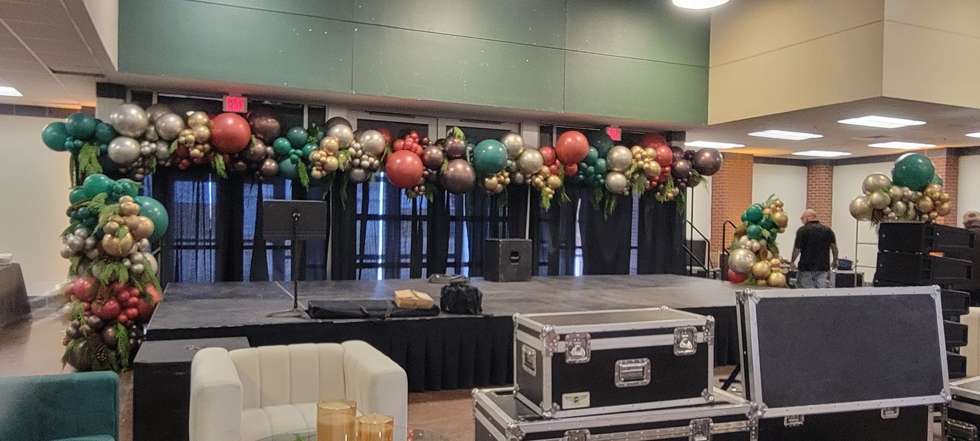 Stage decorated with balloons in a large hall with black curtains and equipment in the foreground.