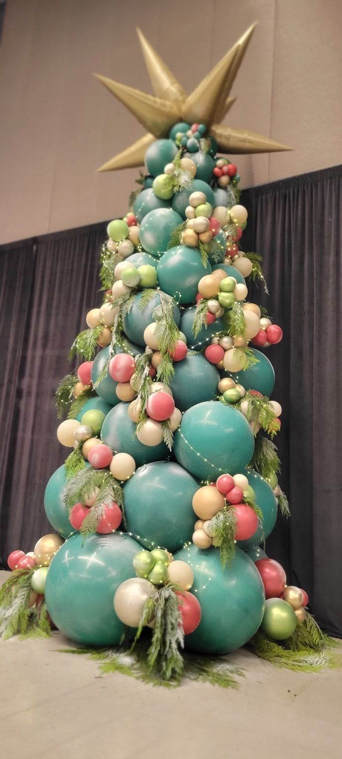 A Christmas tree made of large teal balloons, decorated with smaller colorful balloons and greenery, and a golden star.