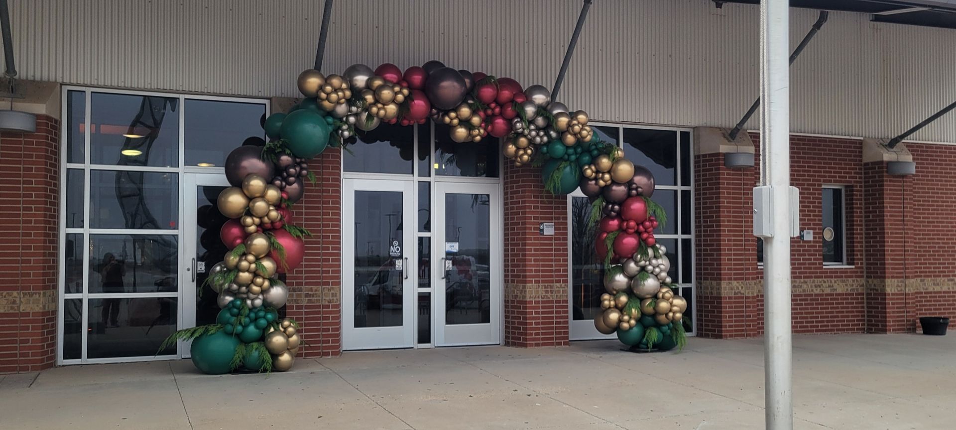 An arched doorway decorated with balloons in green, gold, and burgundy. Building exterior in the background.