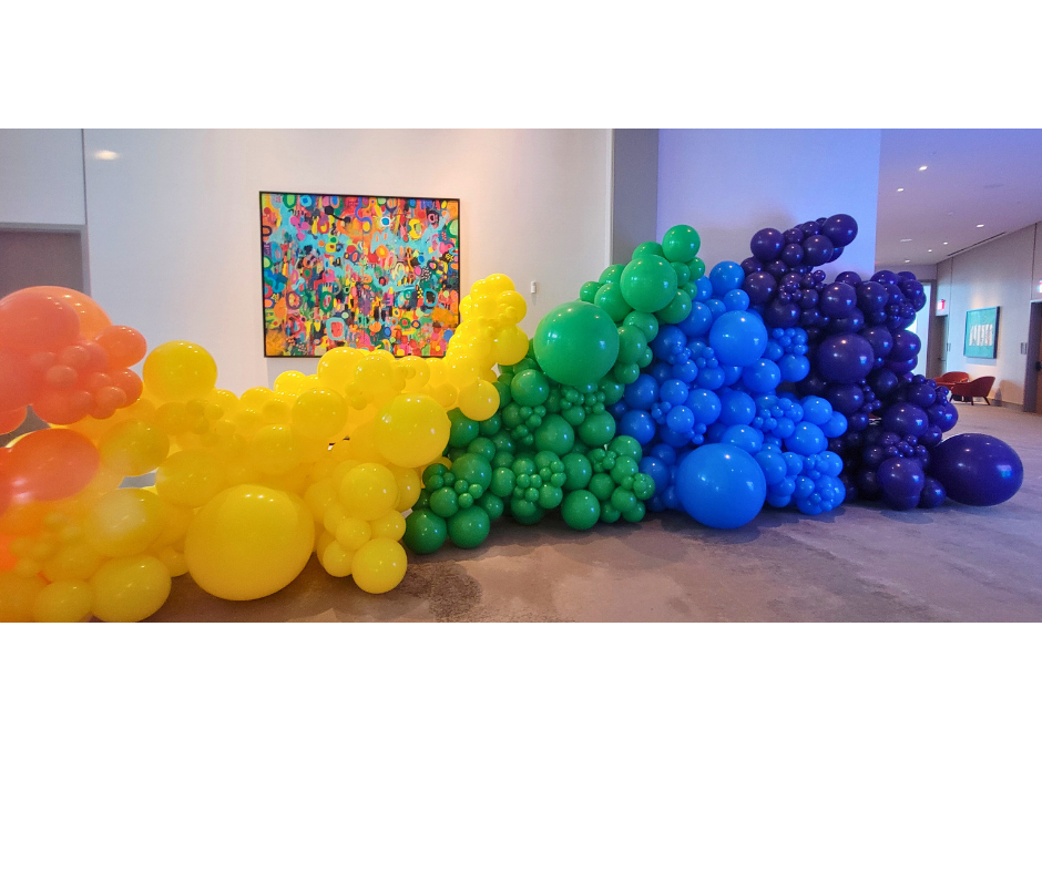 Rainbow-colored balloon arch in an indoor setting; balloons range from orange to purple.