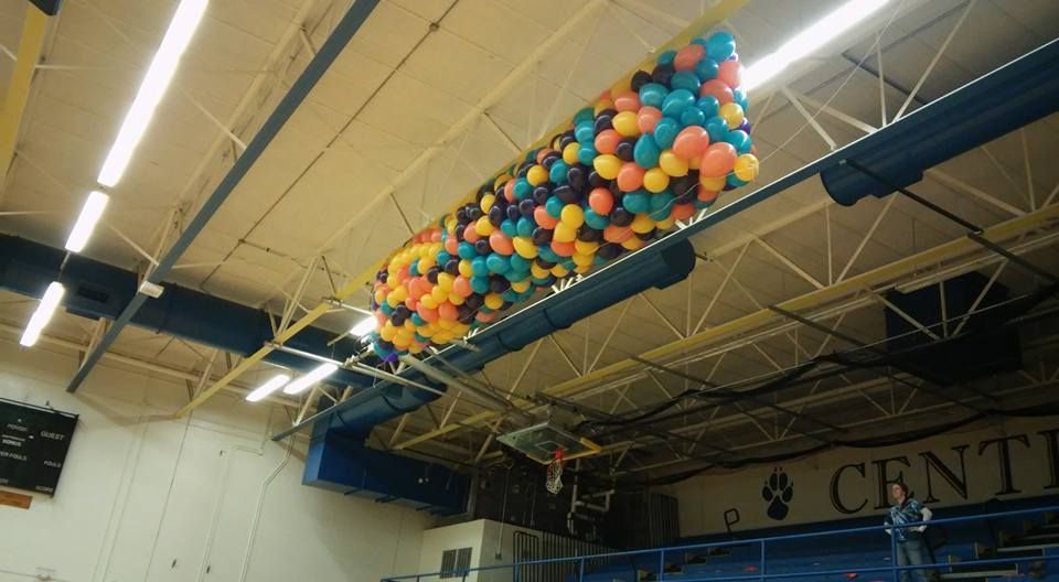 A bunch of balloons are hanging from the ceiling of a gym. Balloon Drop