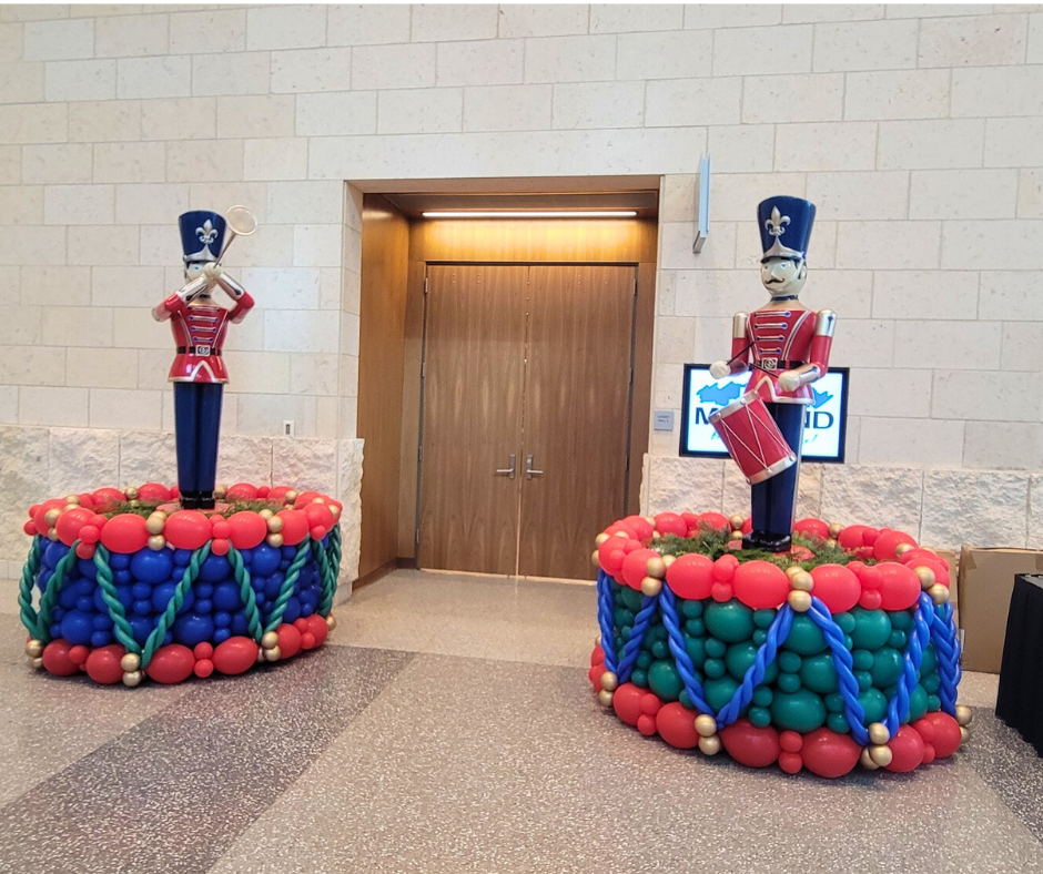 Two toy soldier statues on balloon drums, in front of a wooden door.