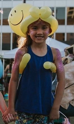 A little girl wearing a balloon hat with a smiley face on it.