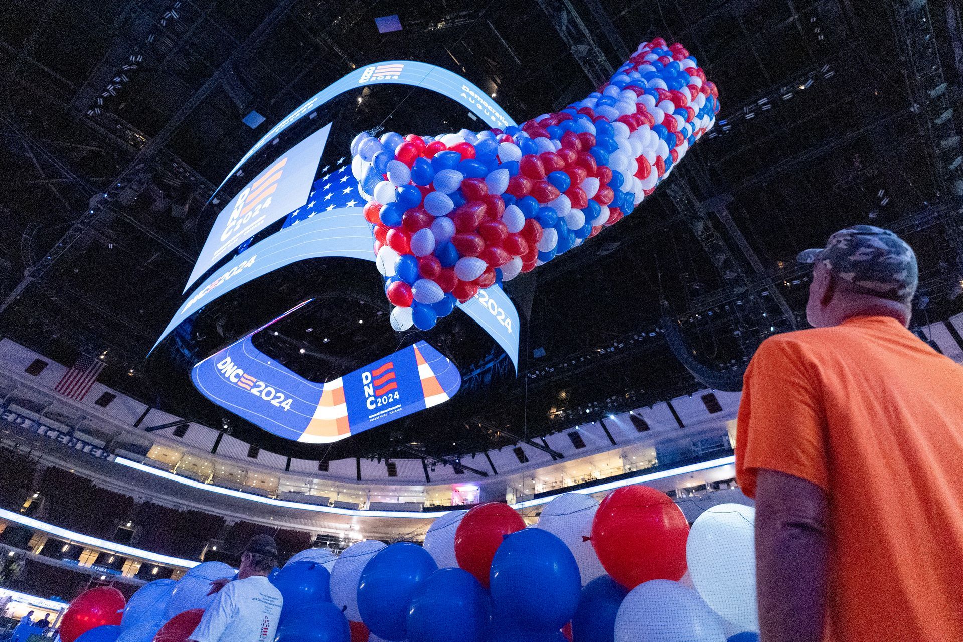 A man in an orange shirt stands in front of a bunch of balloons.  DNC balloon drop