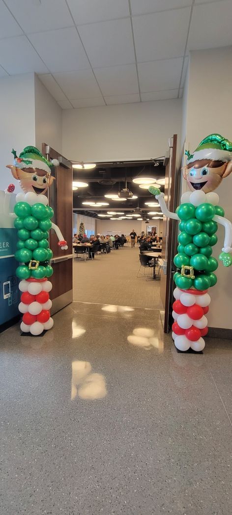 Two balloon elf figures flanking an open doorway. The elves have green and red balloon bodies and elf hats.
