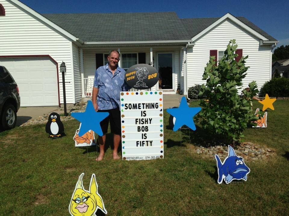 A man stands in front of a sign that says something is fishy bob is fifty