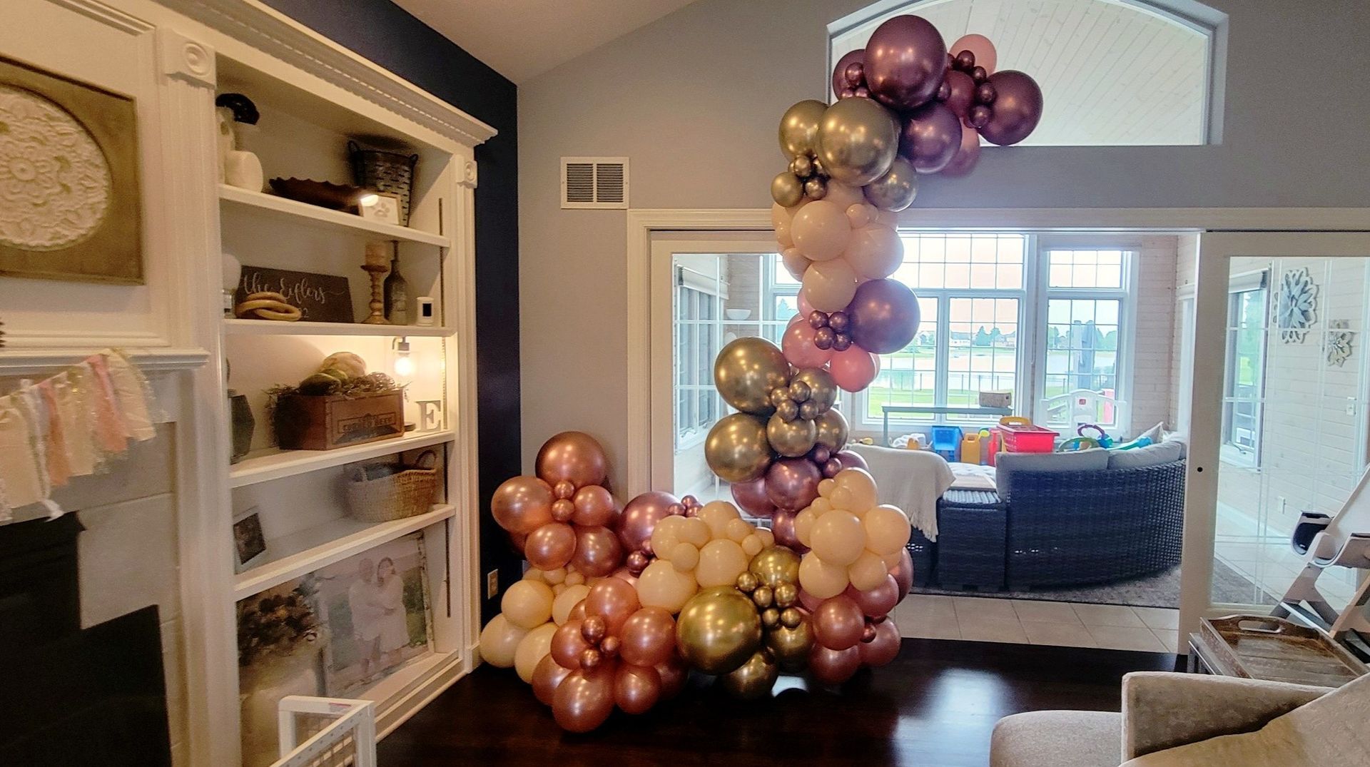 Balloon arch in shades of gold, copper, and purple, framing a doorway.