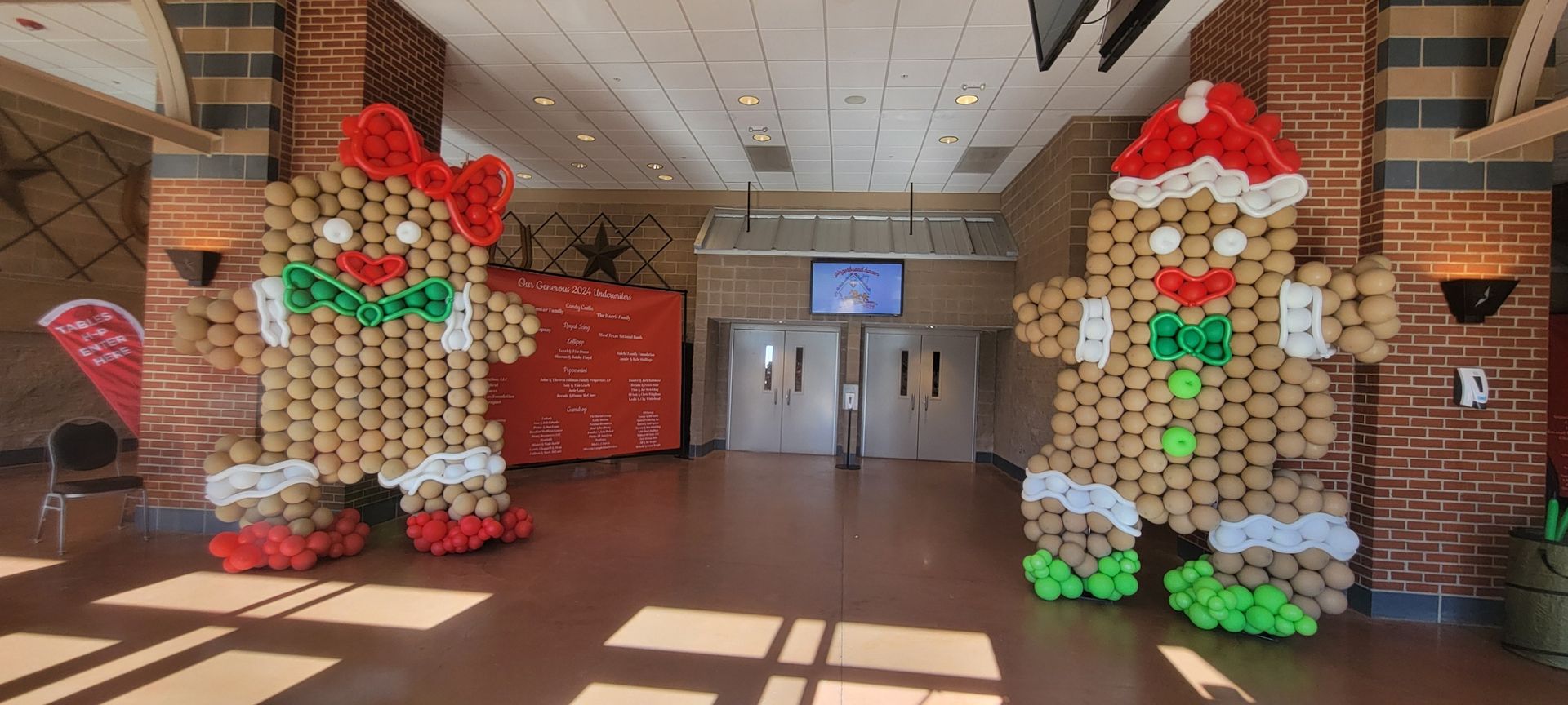 Two gingerbread people decorations made of balloons in a school hallway.
