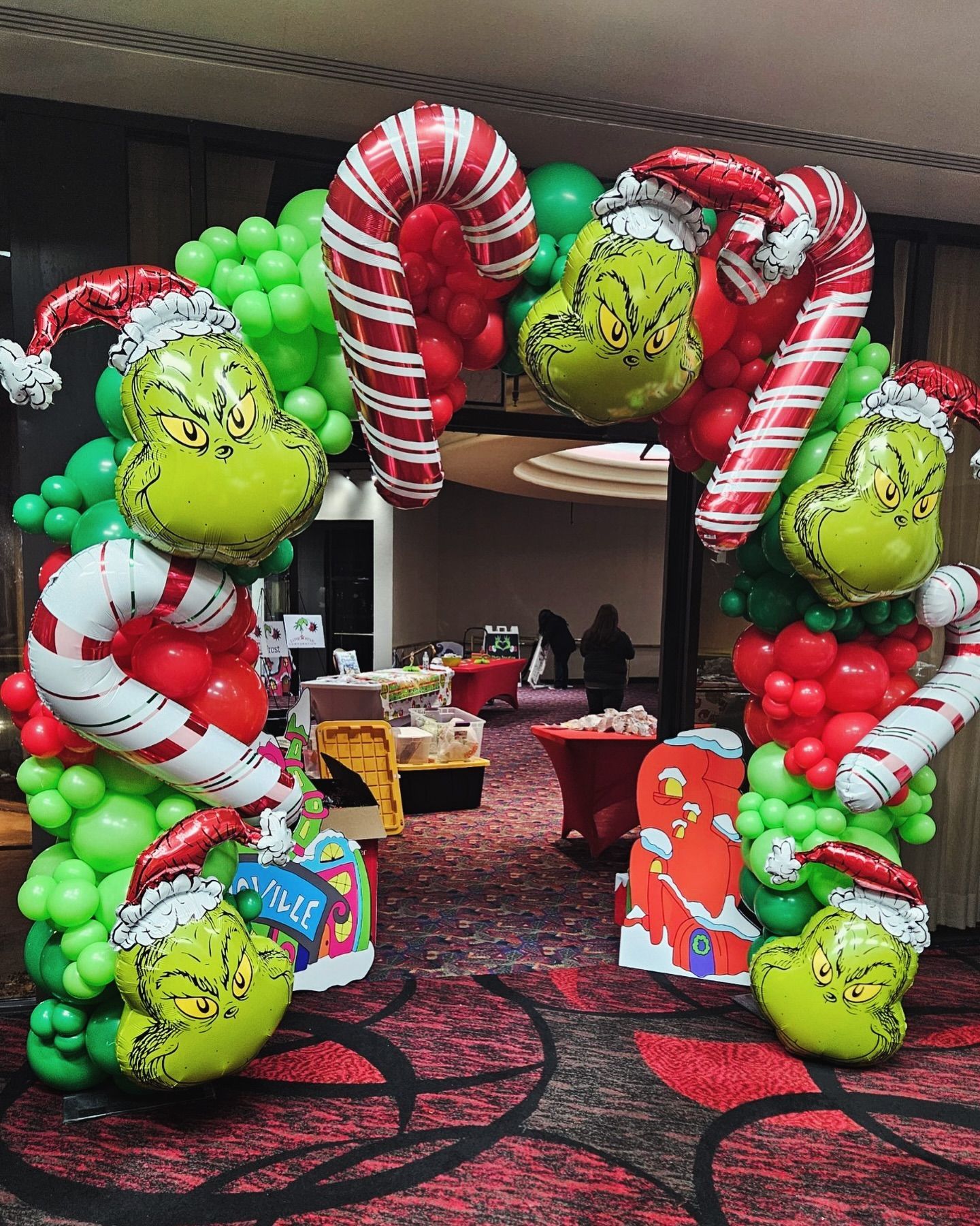 Grinch-themed Christmas balloon arch with Grinch faces and candy canes, indoors.