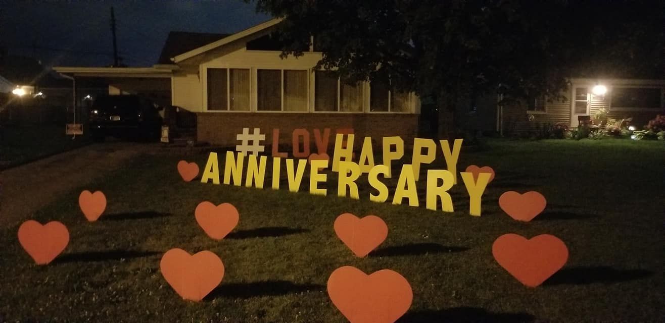 A sign that says happy anniversary with hearts in front of a house.  Heart themed yard card.