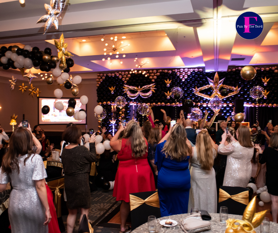 A group of people are dancing in a large room at a party.