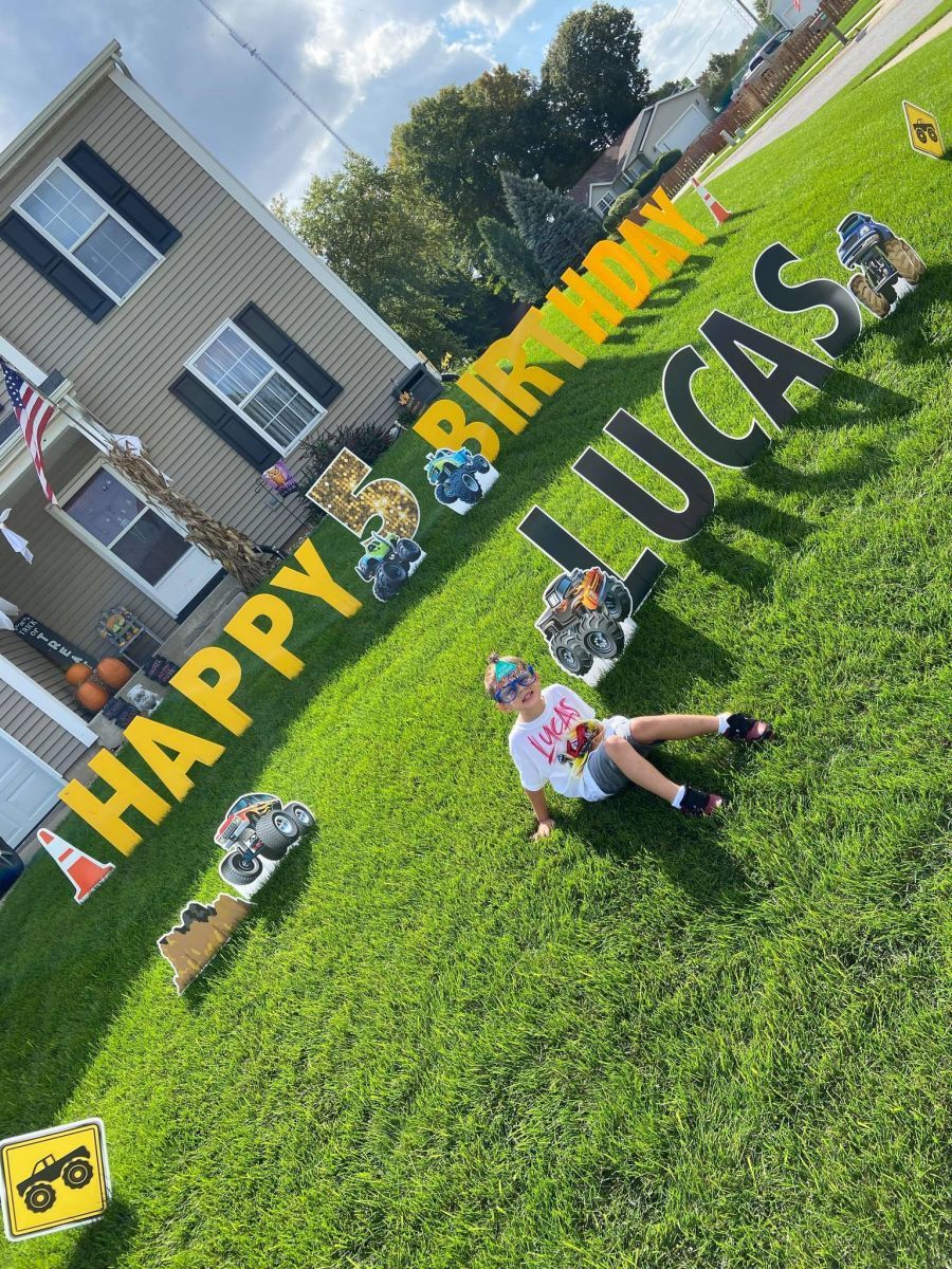 A boy is laying on the grass in front of a sign that says happy birthday lucas.