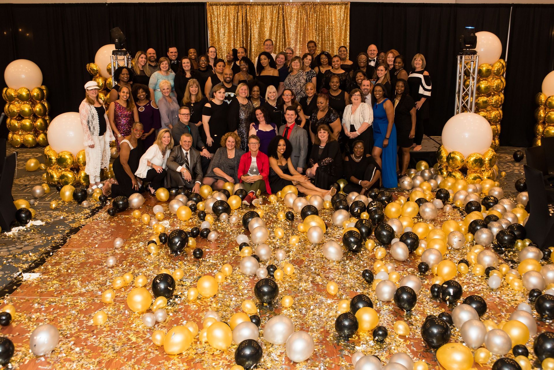A large group of people are posing for a picture in a room filled with balloons and confetti.