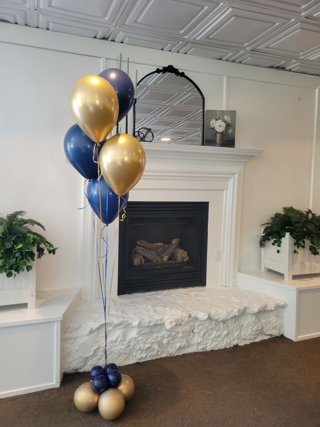 A bouquet of blue and gold balloons are sitting in front of a fireplace.
