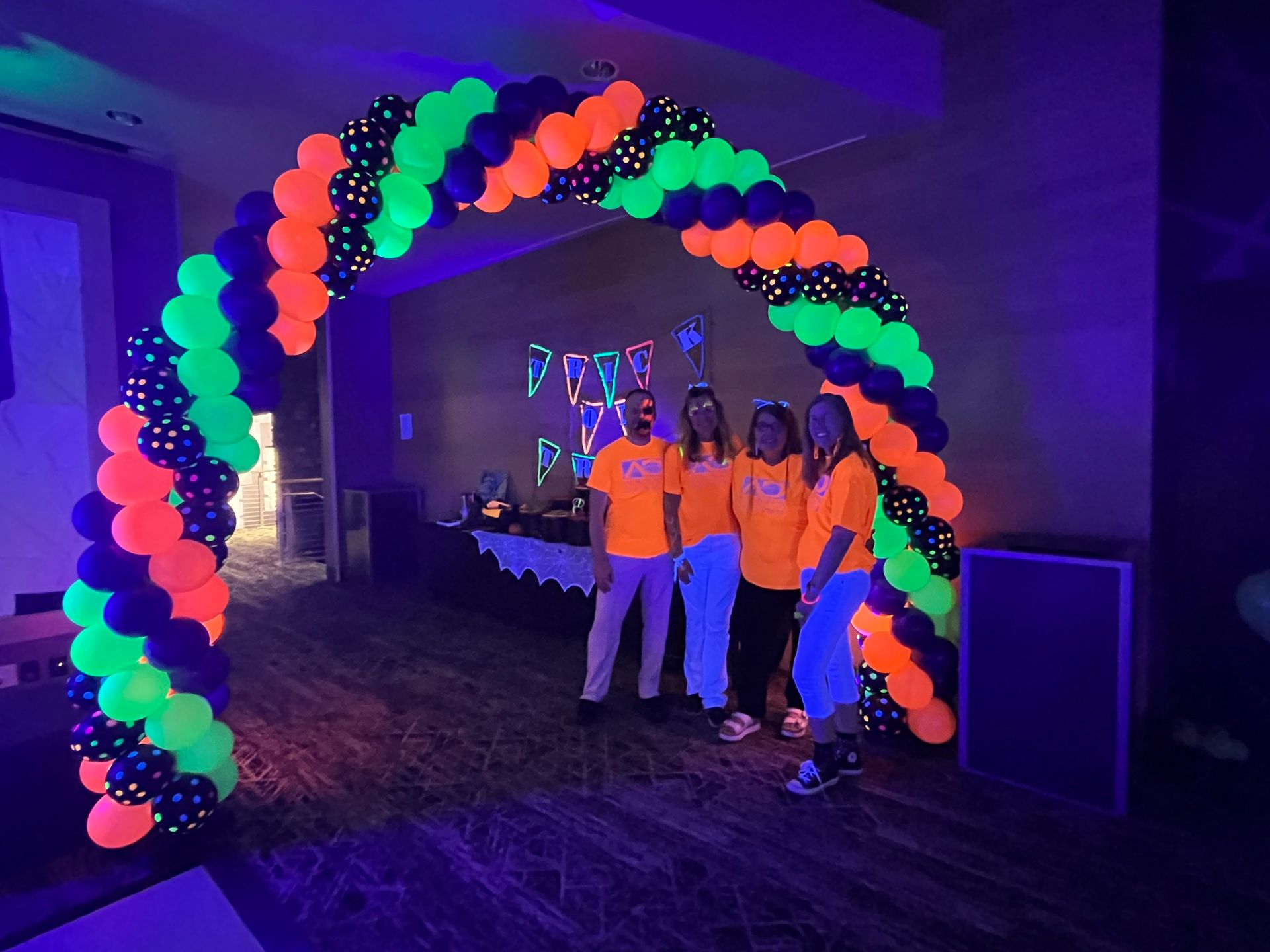A group of people are standing under a glow in the dark neon balloon arch.