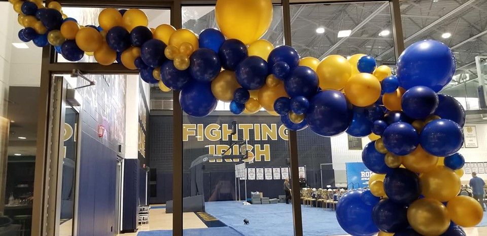 A bunch of blue and yellow balloons are hanging from a window.