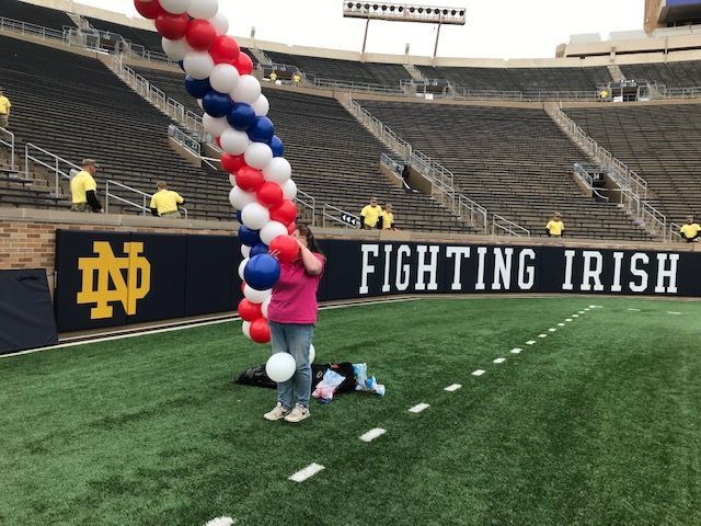 Jenn inflates balloons for a red white and blue arch on the football field at Notre Dame.