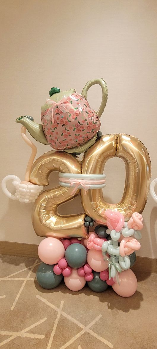 Balloon sculpture of a teapot and the number 20, with pink, gold, and teal balloons.