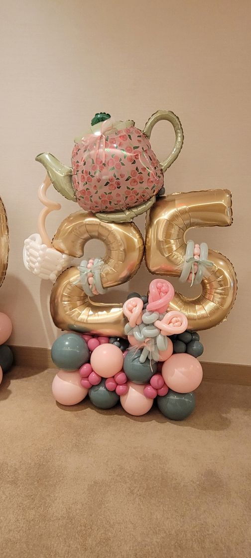 Balloon sculpture of the number 25, with teapot on top. Teal, pink, and gold balloons.
