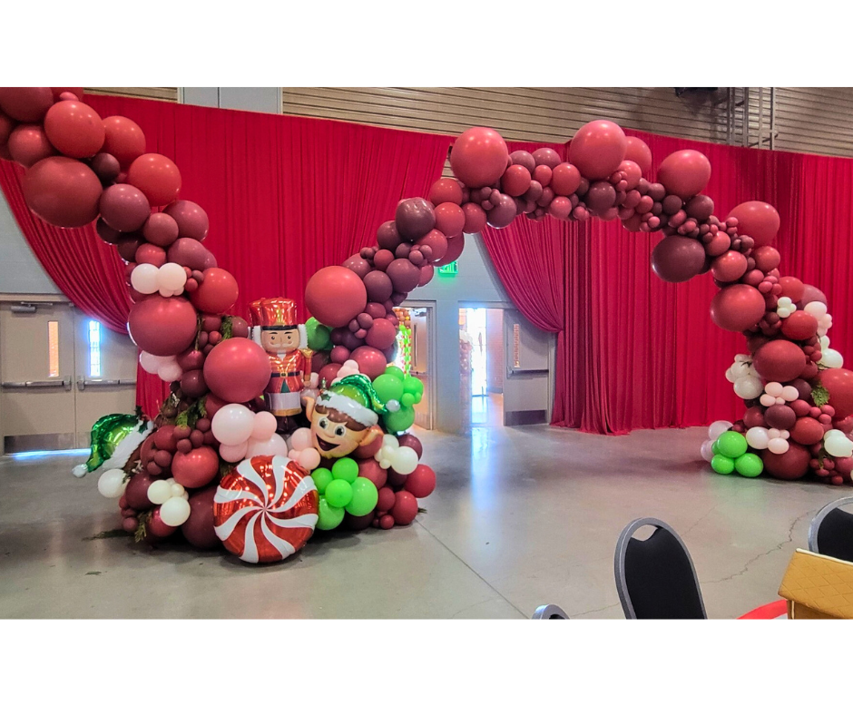 Christmas balloon arch with red, white, and green balloons, a nutcracker, and a giant candy.