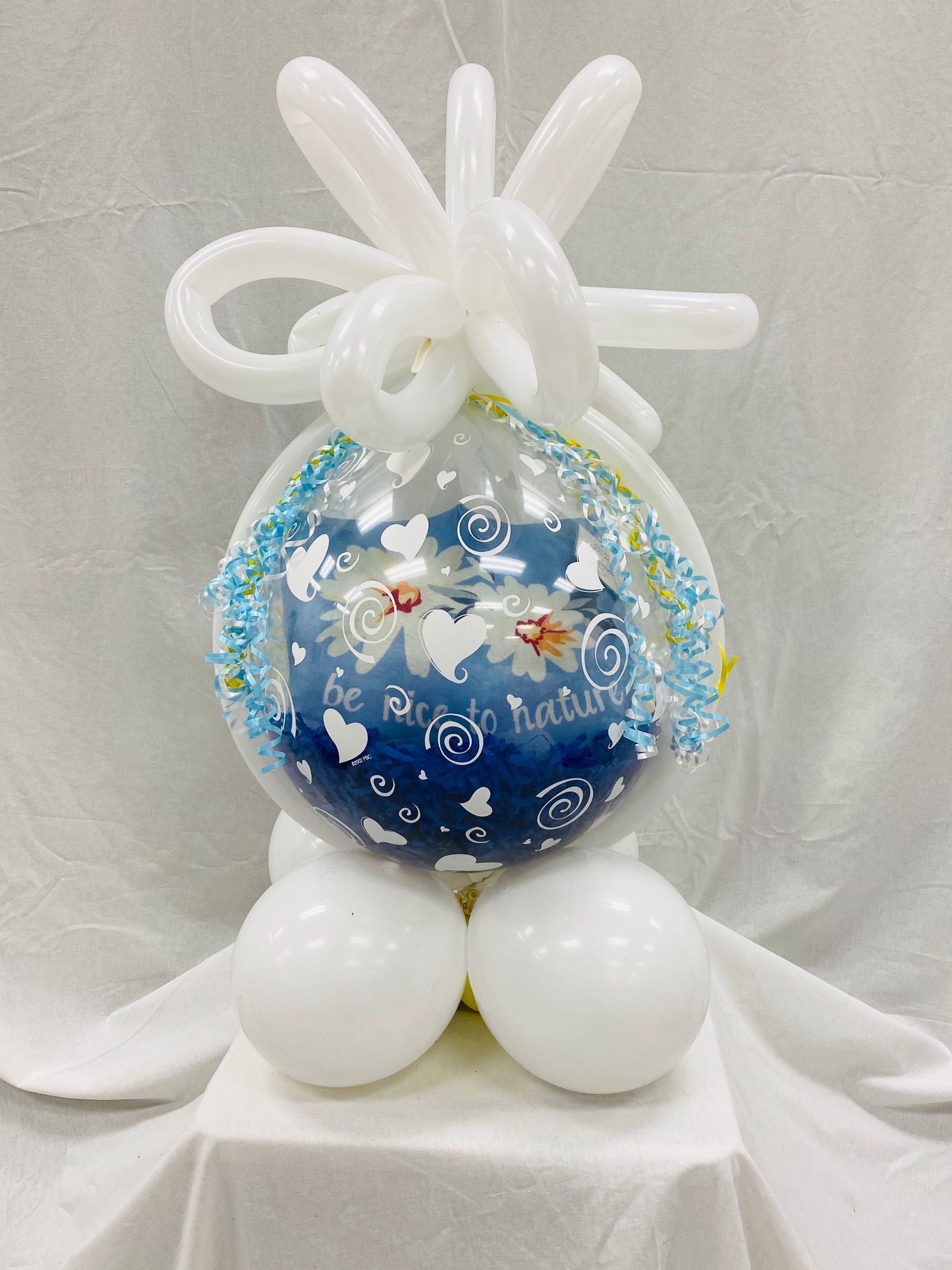 A blue and white balloon is sitting on top of a table surrounded by white balloons.