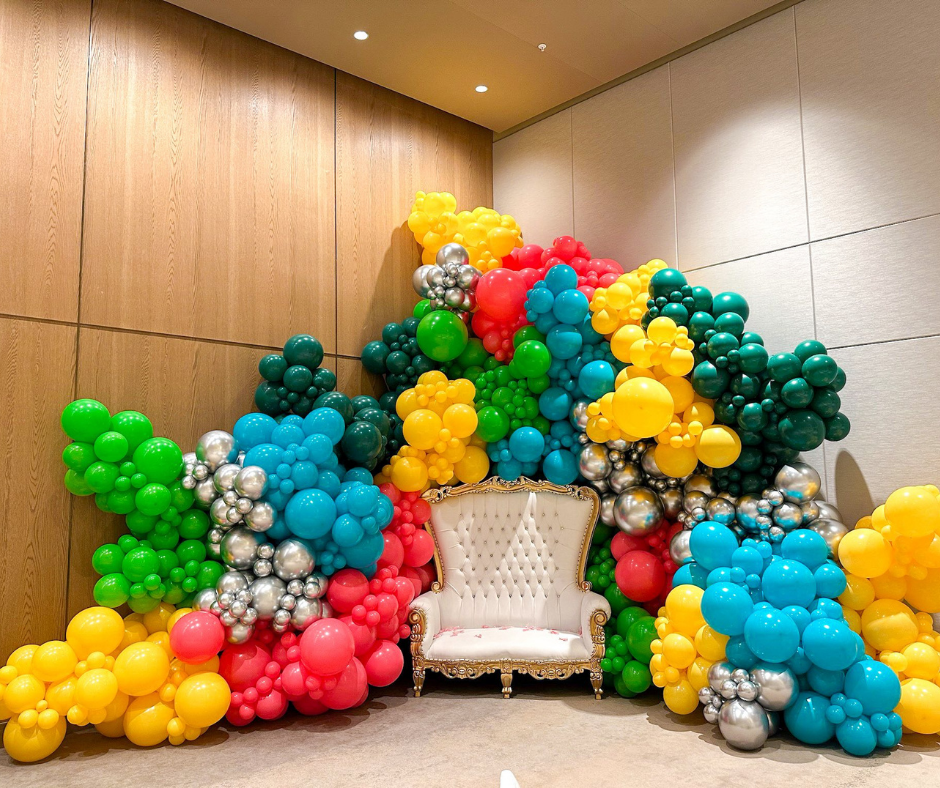 Colorful balloon display surrounding a white ornate chair in a room with wood paneling.