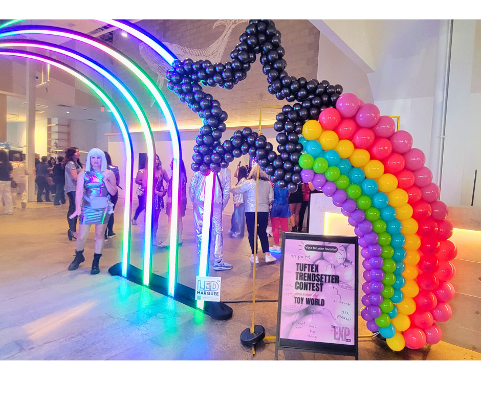 Rainbow archway entrance with balloon star and rainbow, people gathered.