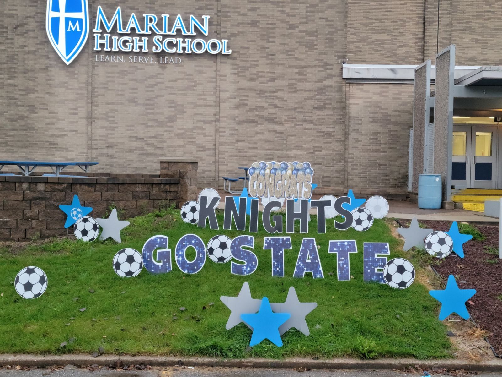 A sign in front of a building that says knights go state.  Soccer themed yard card.