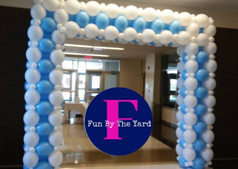A blue and white balloon arch with fun by the yard written on it