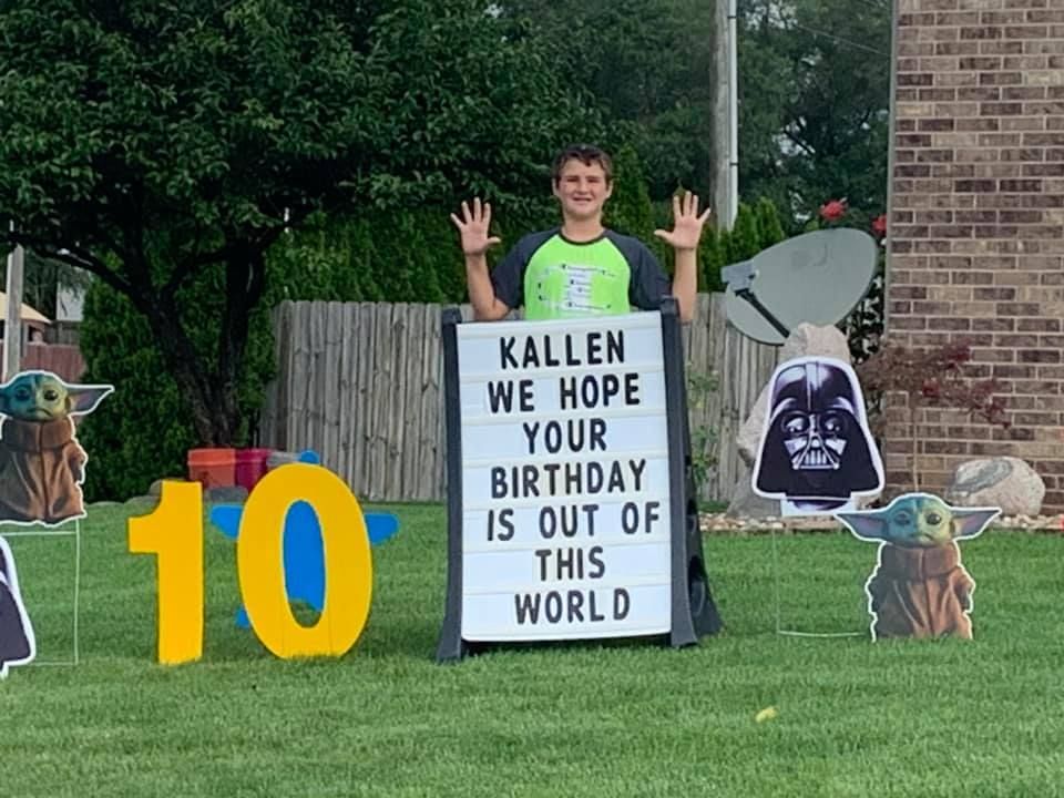 A boy is standing in front of a sign that says `` kallen we hope your birthday is out of this world ''.