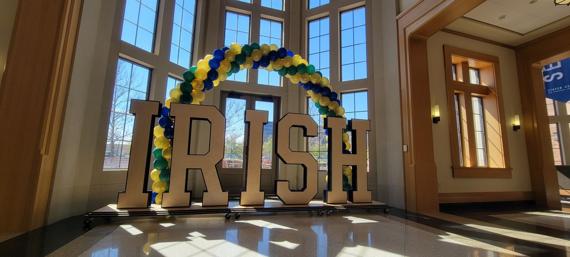 A large wooden sign with the word irish on it is in a hallway with a balloon arch