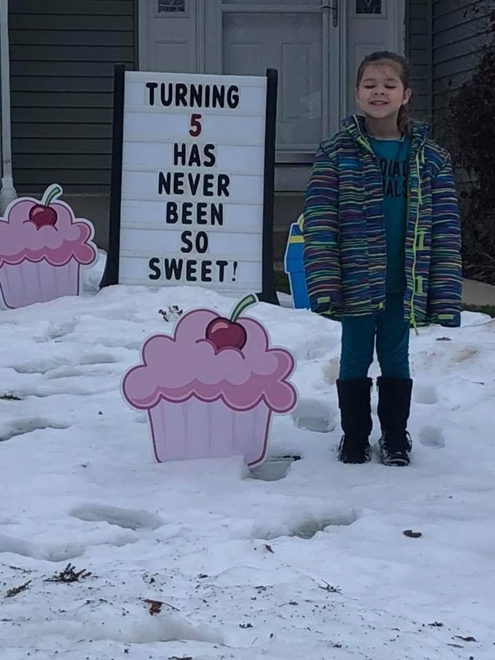 A little girl is standing in front of a sign that says turning 5 has never been so sweet