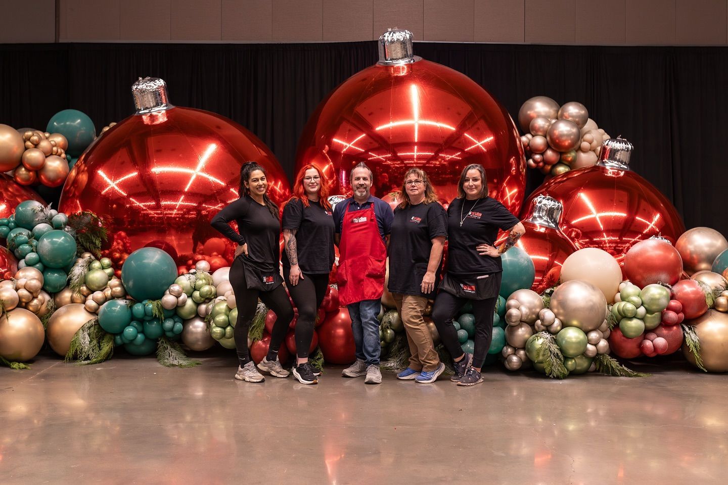 Group of people posing in front of a giant Christmas ornament balloon display.
