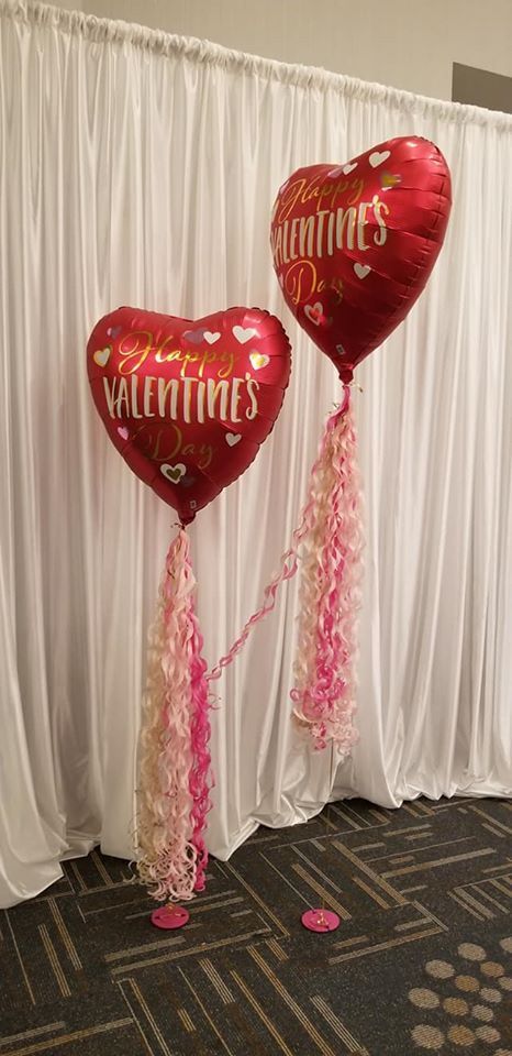 Two heart shaped balloons are sitting in front of a white curtain.