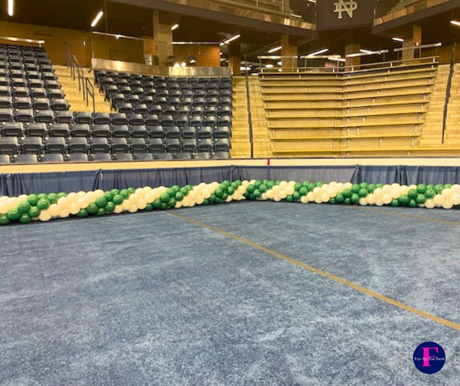 Balloons in green and white along the floor of an arena with blue seating.