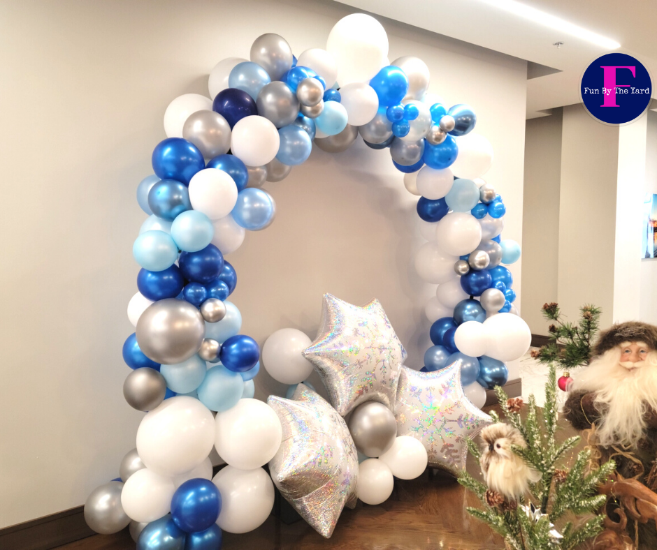 Balloon arch in shades of blue, silver, and white, with star balloons and Christmas decorations.
