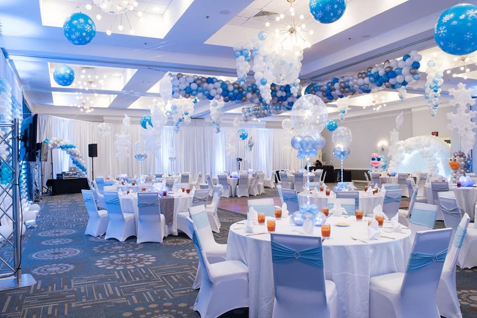 A large room decorated for a party with tables and chairs and balloons hanging from the ceiling.