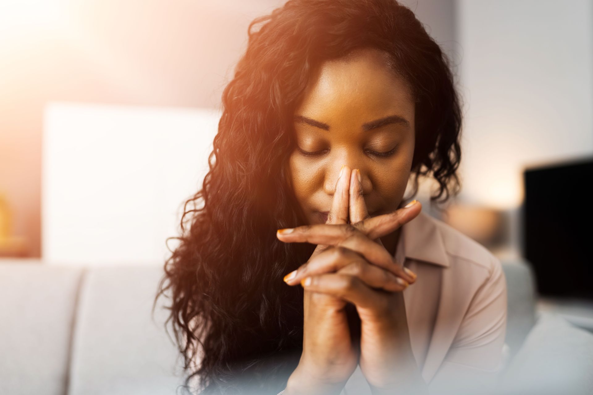 A woman is sitting on a couch with her hands folded in prayer.