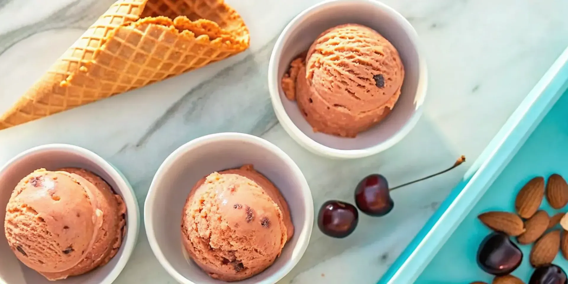 Cherry amaretto ice cream in bowls with fresh cherries, almonds, and a waffle cone.