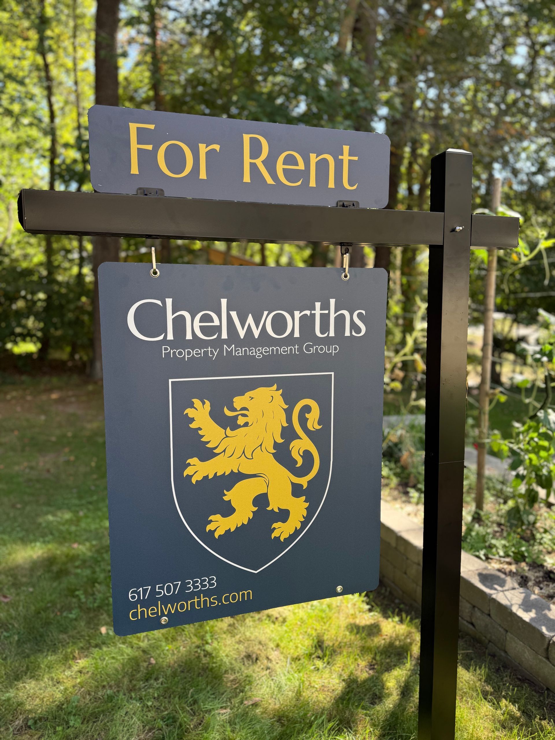 Sign for rent, dark blue with gold text, Chelworths logo of a golden lion, set in grass.