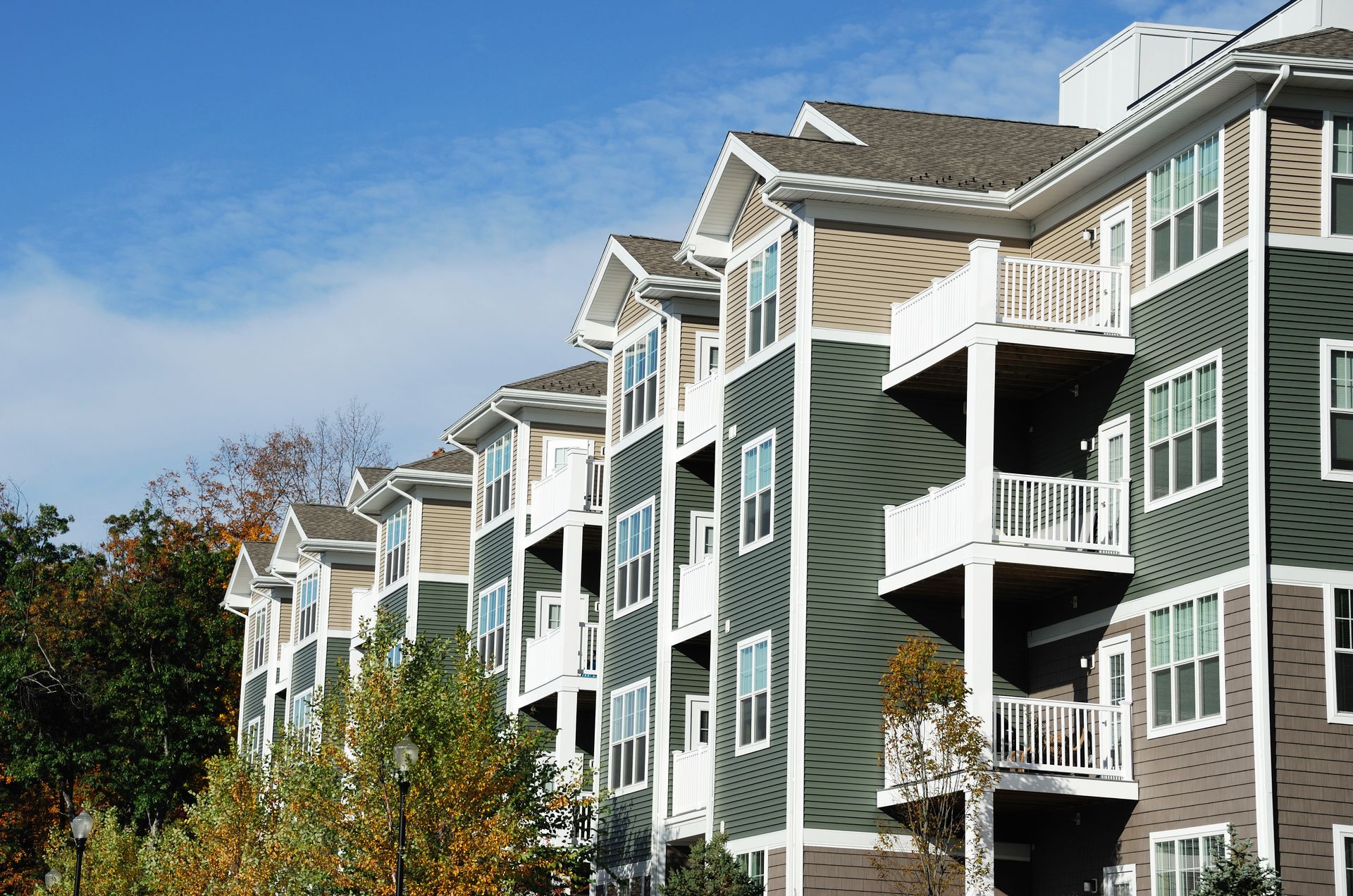 Apartment building with various colored siding, balconies, and gabled roofs under a blue sky.