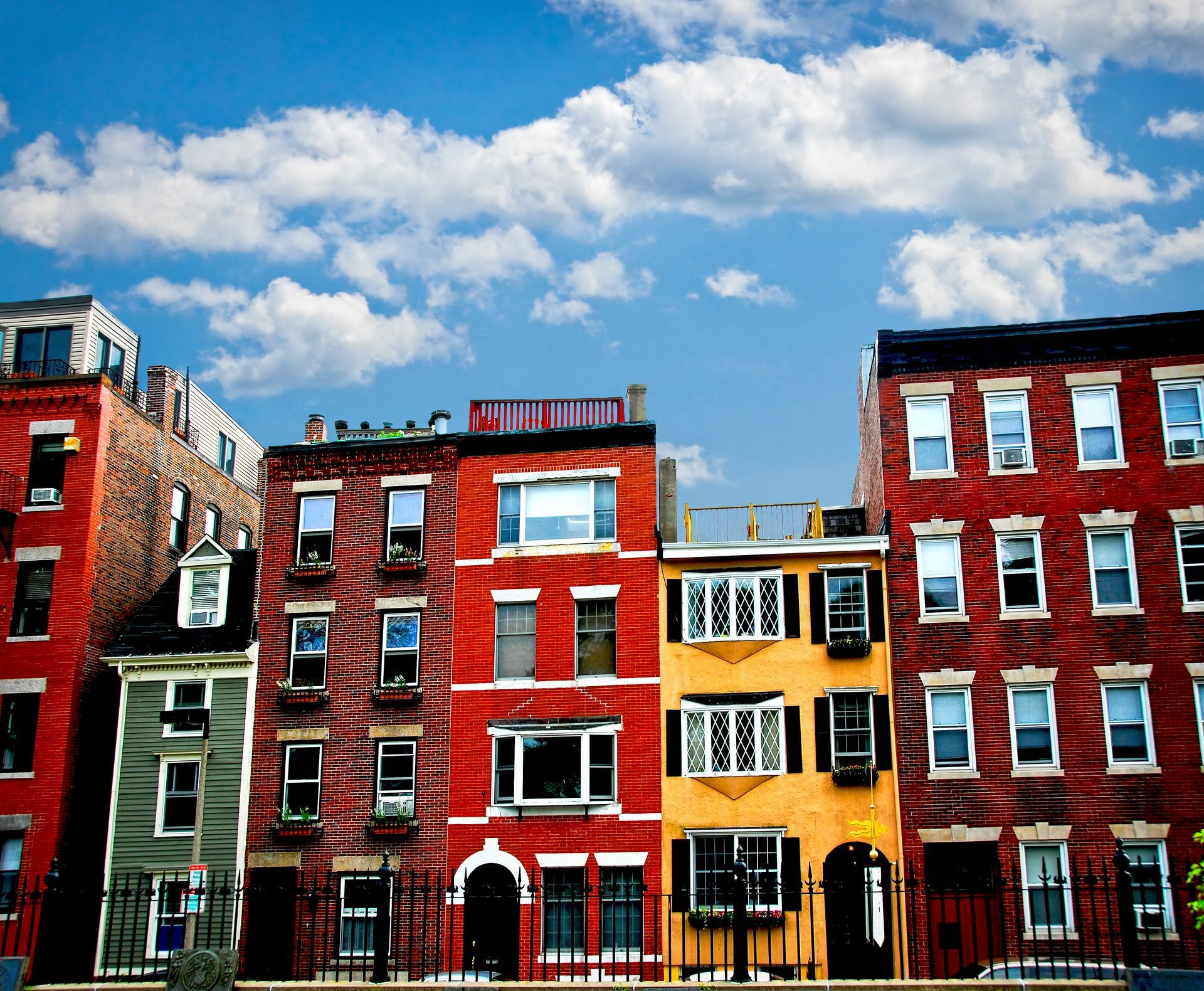 Row of colorful brick townhouses against a cloudy blue sky.