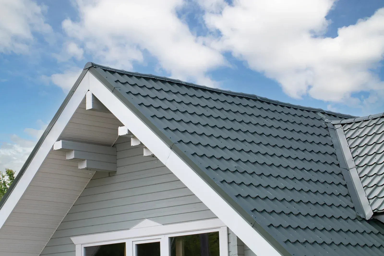 Gray roof on a light blue house with white trim against a cloudy sky.