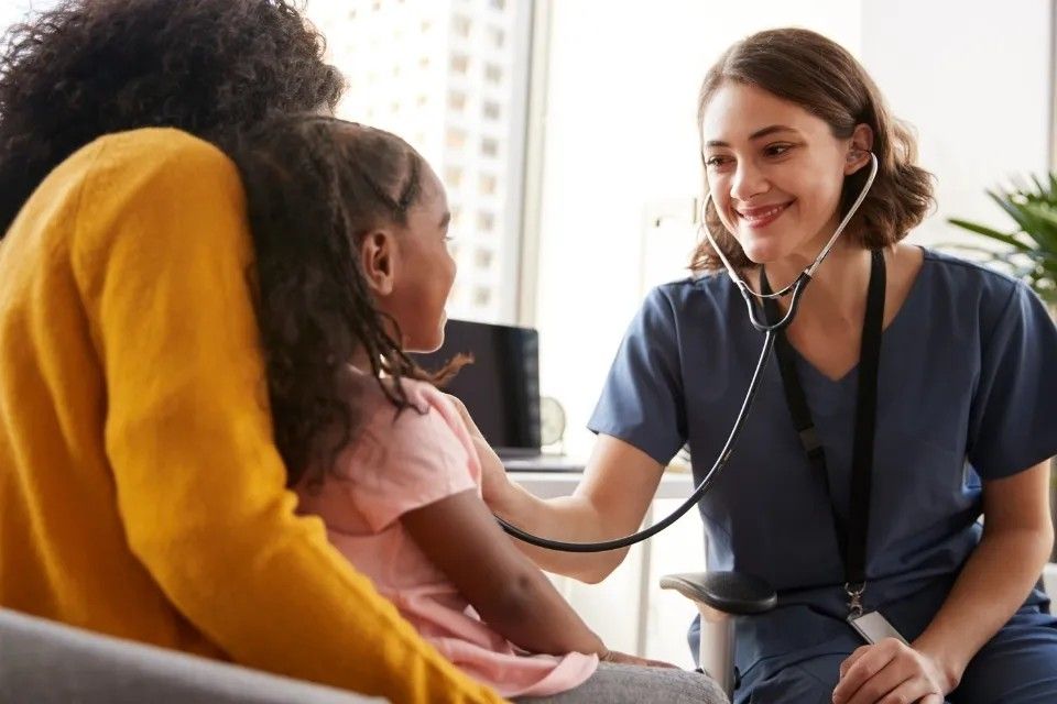 Doctor listening to a child's chest with a stethoscope while the child sits on a parent's lap.