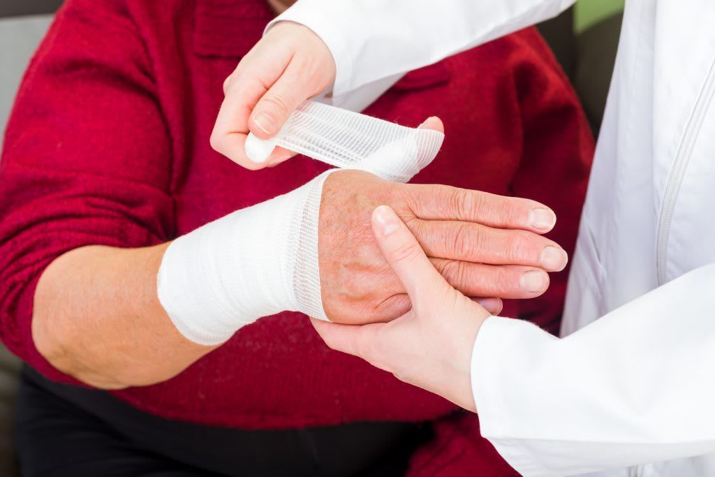 A person's wrist is being wrapped in a bandage by another person in a white coat.