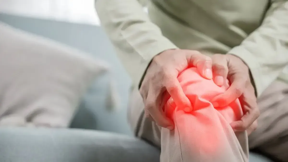 A man is sitting on a couch holding his knee in pain.