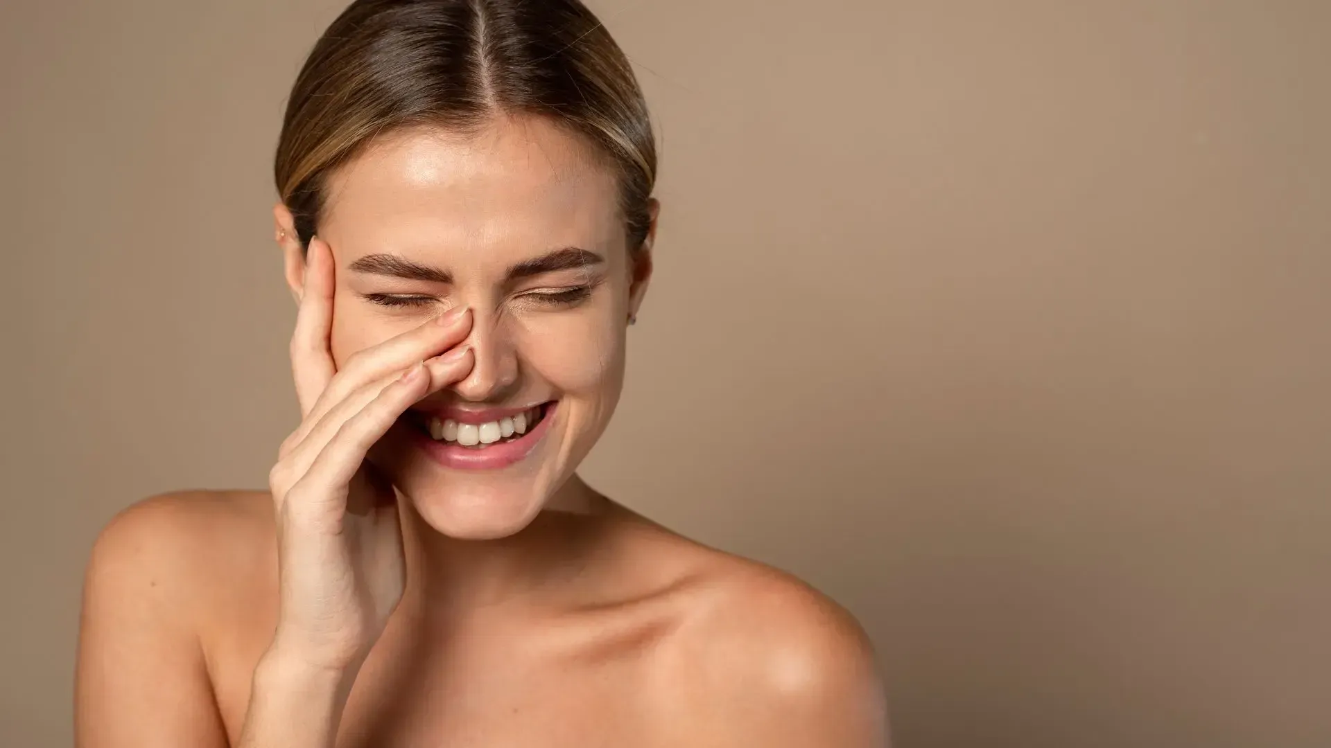 A woman is covering her nose with her hand and smiling.