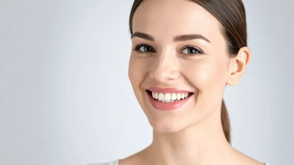 Woman smiling with bright white teeth.  Light skin, brown hair pulled back.  Soft background.