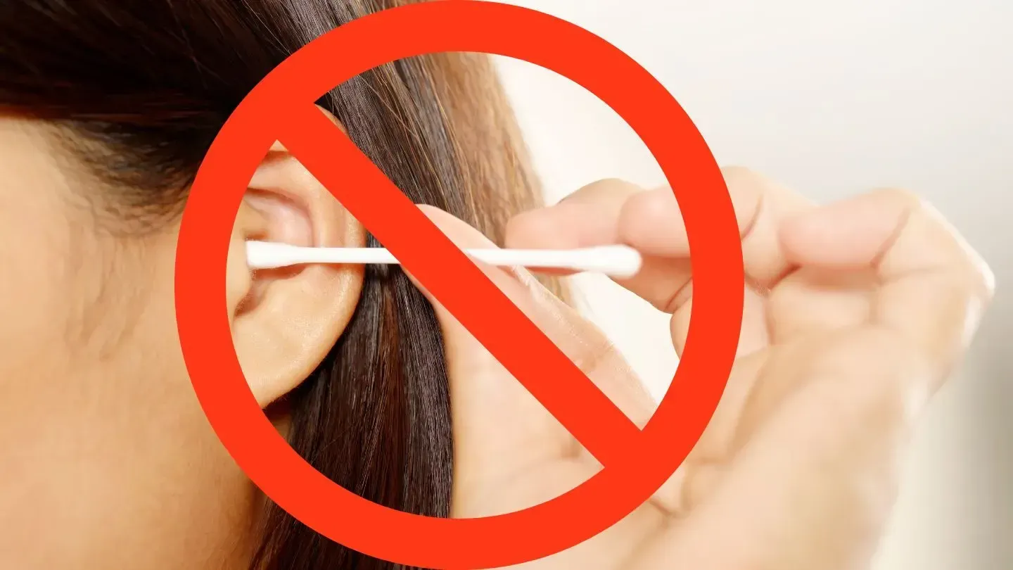 Person's ear with cotton swab, crossed out with a red circle, indicating 