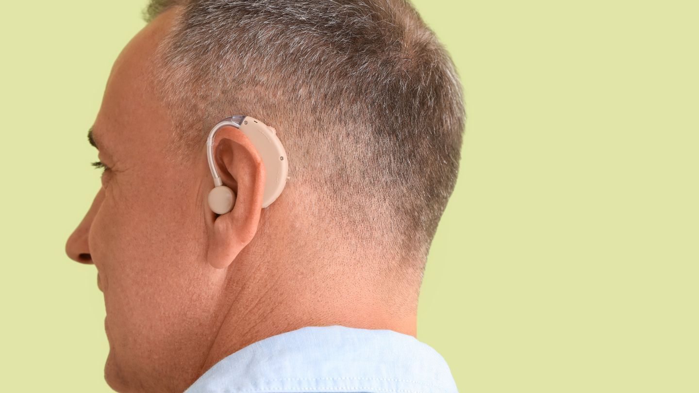 Man wearing a beige hearing aid behind his right ear, side view.